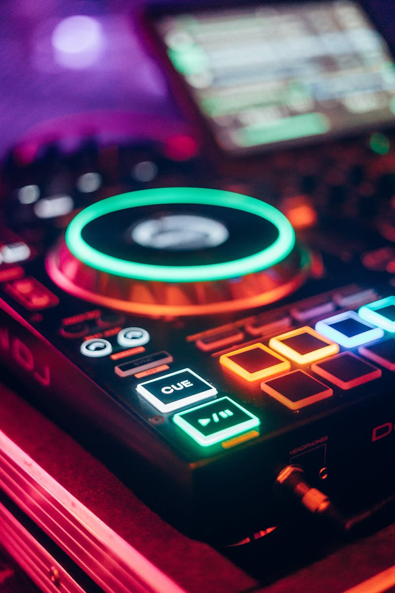 Neon-lit DJ controller with buttons and jog wheel in a vibrant nightclub scene.